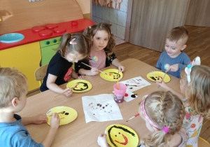 Dzieci przy stoliku malują farbami buźki z uśmiechem