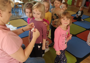 Nauczycielka przykleja dzieciom na ubraniach małe medale z uśmiechniętymi buźkami