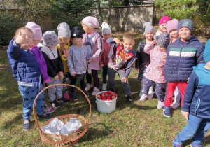 Grupa dzieci stoi przy wiaderku jabłek