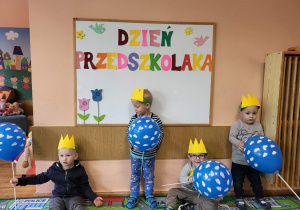 Chłopcy z grupy najmłodszej stoją na tle tablicy Dzień Przedszkolaka.
