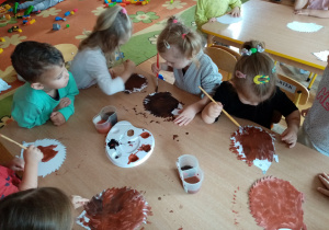 Przedszkolaki wykonują pracę plastyczną- malują sylwetę jeża farbami.