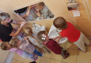 Nauczycielka w łazience pokazuje dzieciom etapy mycia rąk.