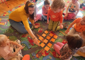 2Nauczycielka wraz z dziećmi układa na dywanie grę „memo obrazkowe”.