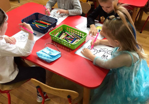 Przedszkolaki kolorują rysunki przedstawiające bajkowe postacie.