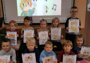 Przedszkolaki prezentują pokolorowane obrazki przedstawiające kota Amadeusza.