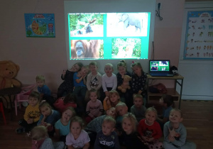 Dzieci z grupy „Promyczki” na tle tablicy przedstawiającej różne zwierzęta.