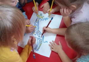 Dzieci kolorują obrazek przedstawiający żyrafę.