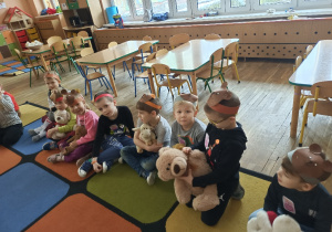 Przedszkolaki siedzą na dywanie ze swoimi pluszowymi misiami