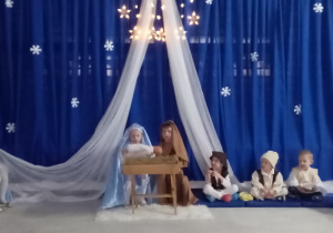 Maryja, Józef oraz pastuszkowie siedzą przy żłóbku.