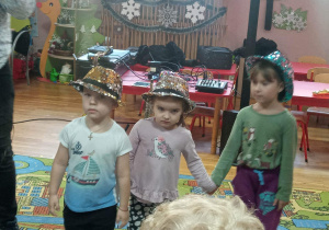 Przedszkolaki w karnawałowych kapeluszach słuchają utworów muzycznych.