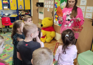 Nauczycielka pokazuje dzieciom rekwizyty związane z Kubusiem Puchatkiem.