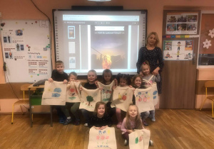 Dzieci wraz z nauczycielką prezentują ozdobione torby płócienne.