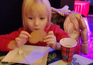 Mikołajowy poczęstunek- dziewczynka je pierniki i pije kakao.