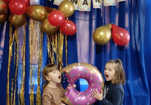 Pamiątkowe zdjęcie dwujki dzieci z dmuchanym balonem w kształcie pączka na tle napisu Tłusty Czwartek