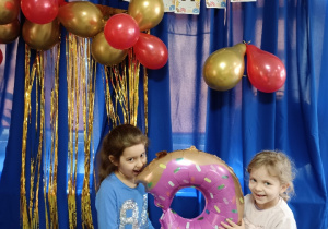 Pamiątkowe zdjęcie dwujki dzieci z dmuchanym balonem w kształcie pączka na tle napisu Tłusty Czwartek
