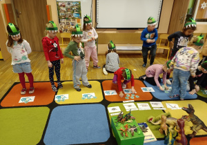Dzieci na dywanie rozwiązują zadania o dinozaurach