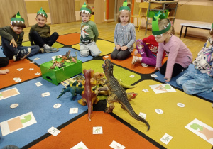 Dzieci na dywanie rozwiązują zadania o dinozaurach