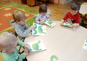 Dzieci tworzą dinozaury z gotowych kart pracy.
