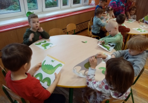 Dzieci tworzą figury dinozaury z gotowych kart pracy.