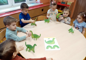 Przedszkolaki bawią się wykonanymi dinozaurami.