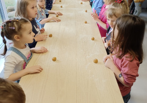 Dzieci stoją przy długim stole na którym leżą kulki ciasta