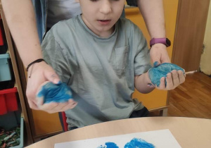 Chłopiec odbija dłonie pomalowane na niebiesko.