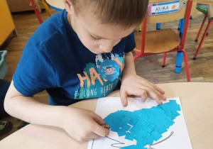 Chłopiec wykleja motyla niebieskim papierem.