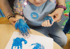 Dziewczynka odbija dłonie pomalowane na niebiesko.