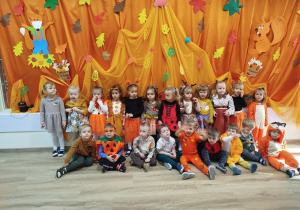 Dzieci z grupy Bąbelków w przebraniach jesiennych na pomarańczowo-jesiennym tle