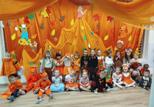 Dzieci z grupy Gwiazdek w przebraniach jesiennych na pomarańczowo-jesiennym tle