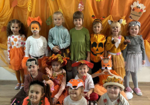 Dzieci z grupy Chmurek w przebraniach jesiennych na pomarańczowo-jesiennym tle