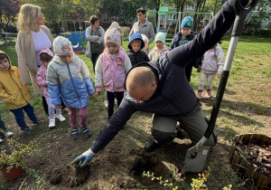 Dzieci w ogrodzie przedszkolnym z nauczycielkami i panem Rafałem sadzom drzewko