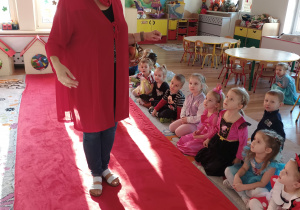 Pani w przebraniu Czerwonego Kapturka idzie po czerwonym dywanie przed dziećmi