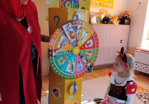 Pani w przebraniu Czerwonego Kapturka i dziewczynka w przebraniu Myszki Miki stoją przy kole zagadek.