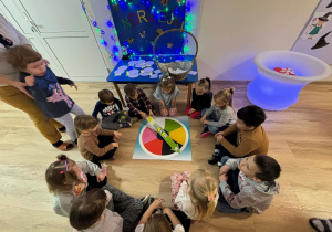 Dzieci siedzą w kole i wróżą sobie na kolorowym kole.