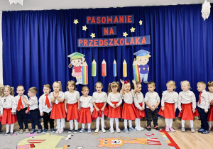 Grupa dzieci stoi na tle dekoracji Pasowania na przedszkolaka.