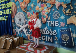 Dziewczynka w stroju biało-czerwonym stoi na podeście na kolorowym tle