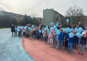 Przedszkolaki z niebieskimi balonami na boisku Szkoły Podstawowej nr 1