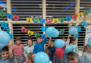 Przedszkolaki z niebieskimi balonami śpiewają hymn "Niebieskie Igrzyska"