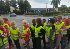 dzieci z grupy 5 w kamizelkach odblaskowych stojące przy skrzyżowaniu typu rondo