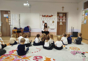 Pani czyta książkę a dzieci siedzą przed nią na dywanie i słuchają