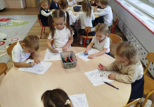 Dzieci siedzą przy stolikach i kolorują obrazki