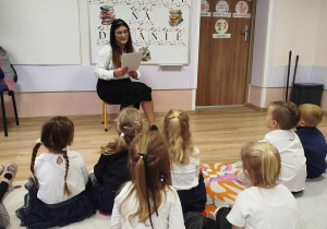 Pani czyta książkę a dzieci siedzą przed nią na dywanie i słuchają